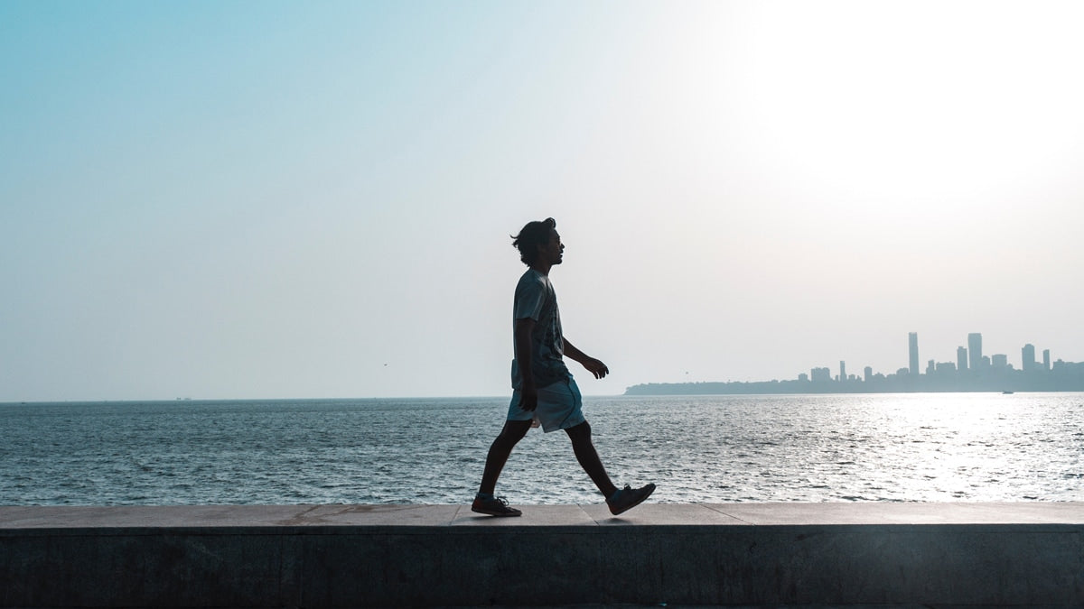 silhouetted man walking on wall with large body of water behind him and city in background