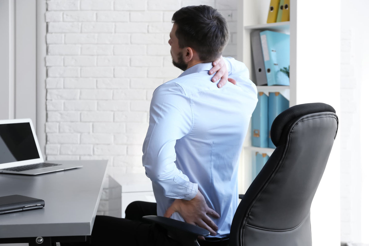 man seated at desk with hands rubbing back and neck