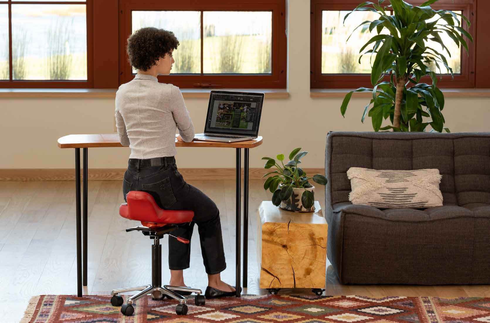 Person using a red QOR360 active chair at a standing-height desk in a bright home office